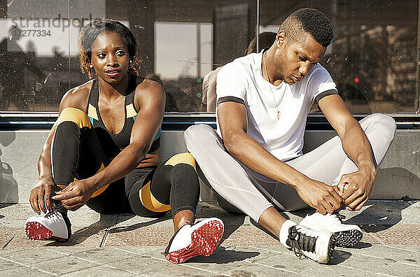 Sportler binden sich die Schnürsenkel  während sie auf dem Bürgersteig der Stadt sitzen