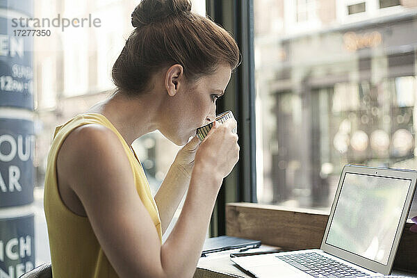 Junge Frau trinkt Kaffee und benutzt einen Laptop in einem Cafe