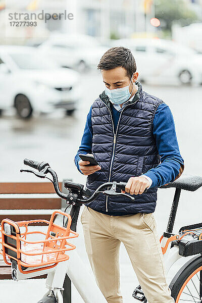 Junger Mann mit Fahrrad  der sein Smartphone benutzt  während er auf der Straße steht