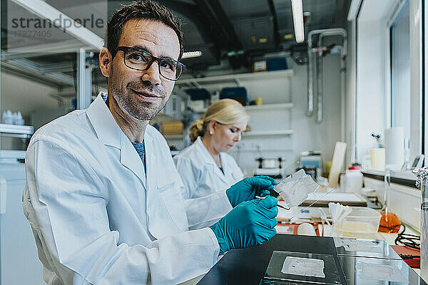 Wissenschaftler  der einen Objektträger für das menschliche Gehirn hält  während er neben einem Mitarbeiter im Labor sitzt