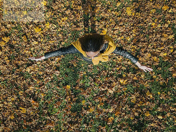 Frau mit ausgestreckten Armen  die auf trockenen Blättern steht  während sie sich im Herbst im Park vergnügt