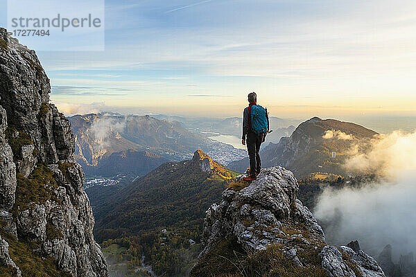 Nachdenklicher Wanderer  der die Aussicht betrachtet  während er bei Sonnenaufgang auf einem Berggipfel in den Bergamasker Alpen  Italien  steht