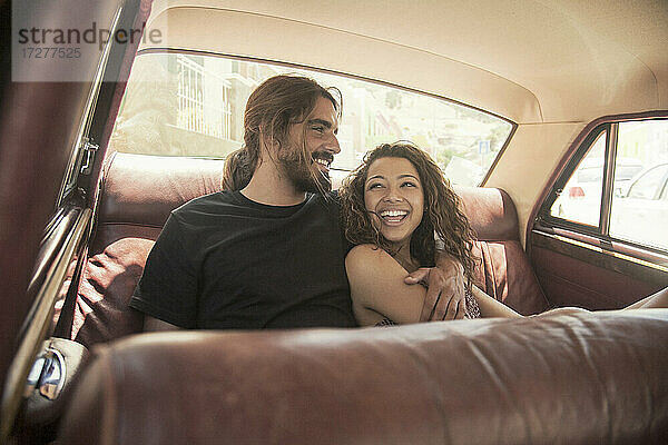 Junges Paar lacht bei der Entspannung im Auto an einem sonnigen Tag