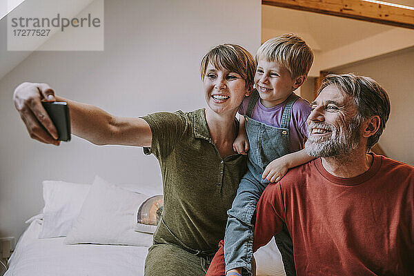 Glückliche Mutter  die ein Selfie mit ihrem Smartphone macht  während Vater und Sohn daneben sitzen