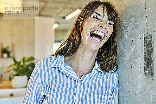 Frau lachend  während sie sich zu Hause an die Wand lehnt