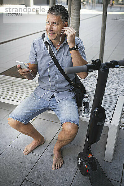 Älterer Mann hört Musik über Kopfhörer  während er auf einer Bank sitzt