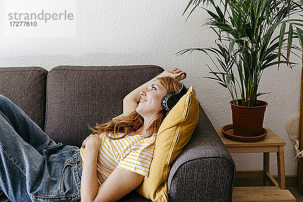 Junge Frau hört Musik über Kopfhörer  während sie zu Hause auf dem Sofa liegt