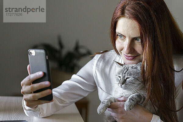 Junge Frau nimmt Smartphone Selfie mit Katze auf dem Schoß