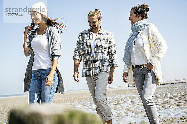 Lächelnde Frau  die mit ihrem Freund und ihrer Mutter am Strand spazieren geht
