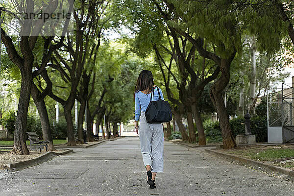 Rückansicht einer Frau mit Handtasche auf dem Fußweg im Park