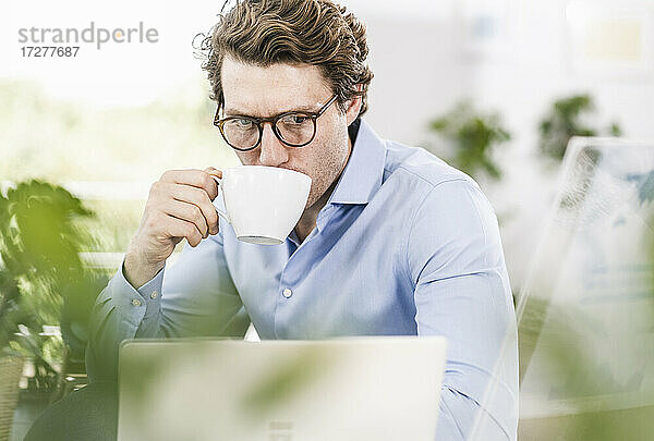 Mittlerer erwachsener Mann  der am Laptop arbeitet und Kaffee trinkt  während er im Büro sitzt