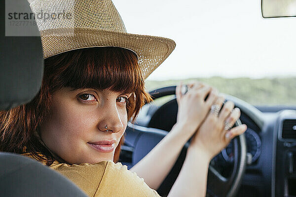 Nahaufnahme einer jungen  schönen  rothaarigen Frau mit Hut  die im Auto sitzt