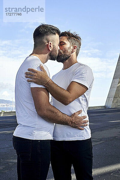Zärtliches schwules Paar küsst sich auf einer Brücke gegen den Himmel