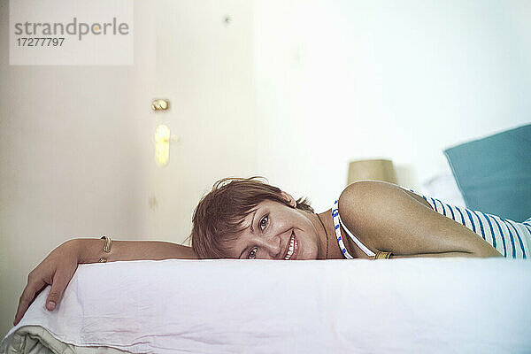 Lächelnde junge Frau auf dem Bett liegend zu Hause