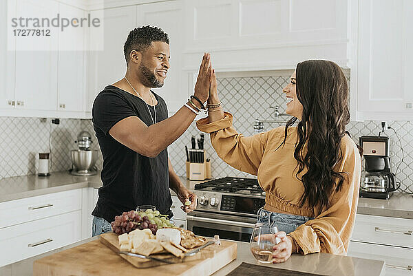 Lächelnder Mann und lächelnde Frau  die sich in der Küche zu Hause die Hand reichen
