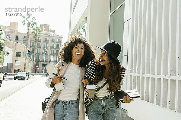 Geschäftsfrauen lachen beim Spaziergang auf der Straße an einem sonnigen Tag