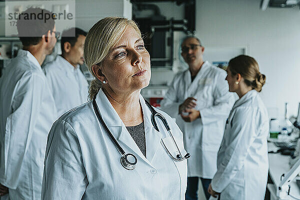 Wissenschaftlerin schaut weg  während sie mit einem Mitarbeiter im Hintergrund in einem Labor steht