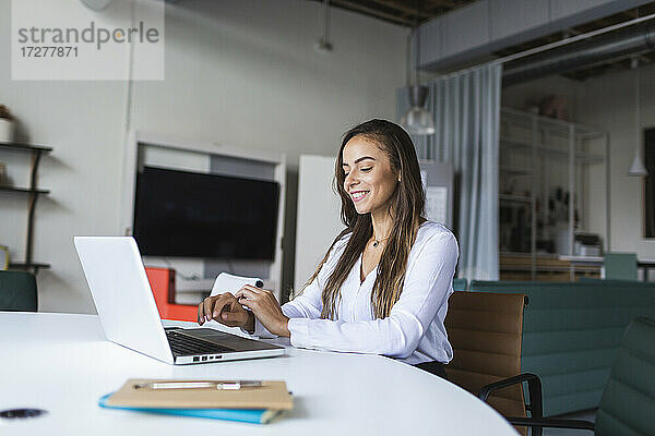 Lächelnde Geschäftsfrau  die am Schreibtisch im Büro einen Laptop benutzt
