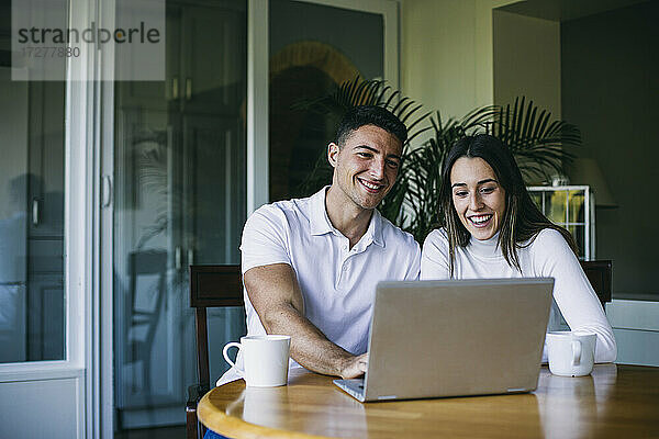 Lächelnder Freund und Freundin trinken Kaffee und benutzen einen Laptop zu Hause