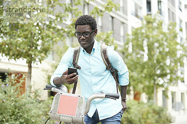 Mann  der sein Smartphone benutzt  während er mit dem Fahrrad in der Stadt steht