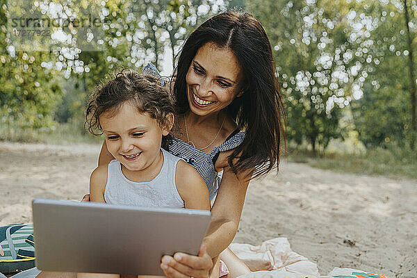 Lächelnde Mutter und Tochter mit digitalem Tablet am Strand