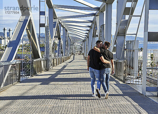 Homosexuelles Paar küsst sich beim Spaziergang auf einer Brücke an einem sonnigen Tag