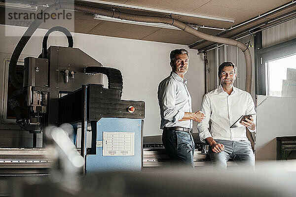Lächelnder männlicher Ingenieur mit digitalem Tablet bei einem Kollegen in der Industrie
