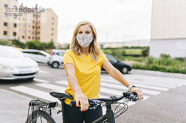 Frau mit Gesichtsschutzmaske steht mit Fahrrad auf der Straße in der Stadt