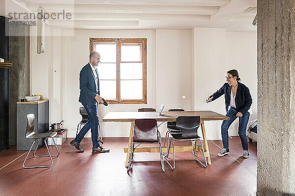 Unbeschwerter Mann und Frau spielen Tischtennis  während sie im Büro stehen