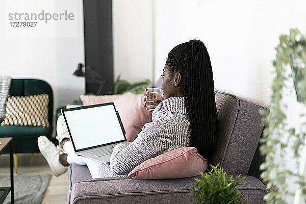 Junge Geschäftsfrau  die Wasser trinkt und am Laptop arbeitet  während sie zu Hause sitzt