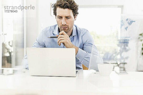 Mittlerer erwachsener Mann  der sich bei der Arbeit am Laptop im Büro konzentriert