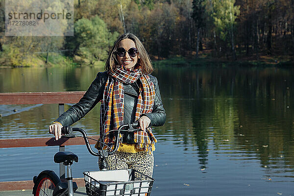 Lächelnde Frau mit Fahrrad auf Pier über See