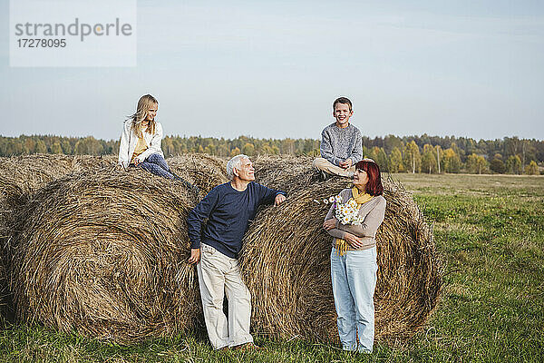 Älteres Ehepaar mit Enkelkindern auf Heuballen auf einem Feld sitzend am Wochenende