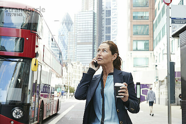 Geschäftsfrau mit Kaffeetasse  die in der Stadt steht und mit ihrem Handy telefoniert