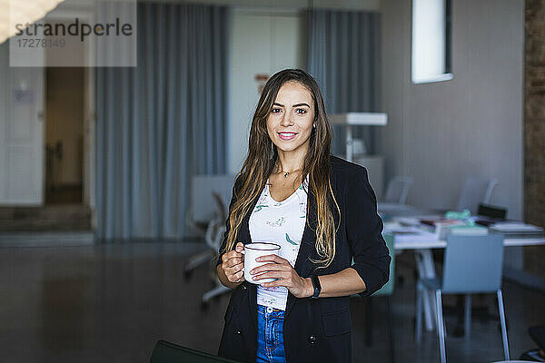 Lächelnde Geschäftsfrau mit Kaffeebecher im Büro