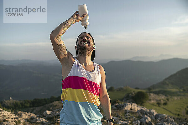 Sportler  der sich Wasser ins Gesicht gießt  während er auf einem Berg gegen den klaren Himmel steht