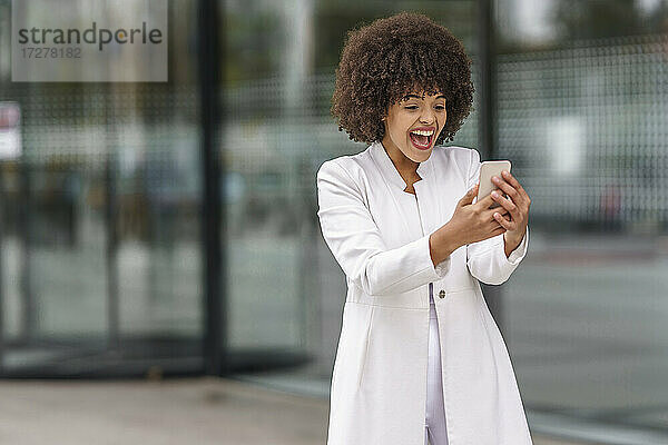 Junge Geschäftsfrau  die im Freien stehend ein Mobiltelefon benutzt