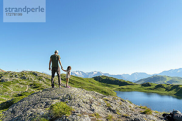 Vater und Tochter stehen auf einem Felsen und betrachten die Aussicht gegen den klaren Himmel