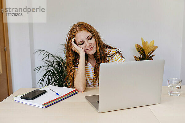 Junge Frau mit Hand in den Haaren  die einen Laptop benutzt  während sie zu Hause sitzt