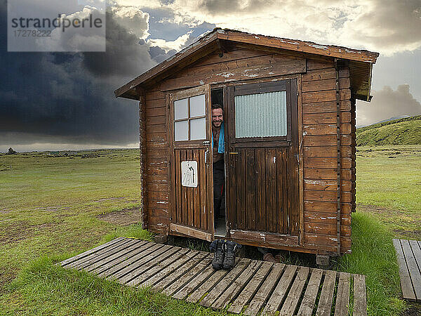 Lächelnder männlicher Tourist  der aus der Tür eines Holzhauses blickt
