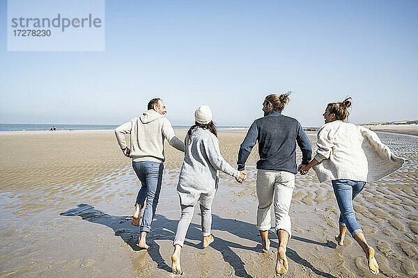 Familie hält sich beim Laufen am Strand an den Händen