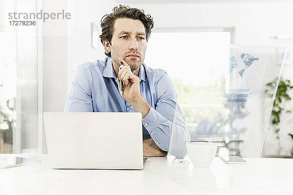 Mittlerer erwachsener Mann  der im Büro sitzend auf ein Whiteboard schaut