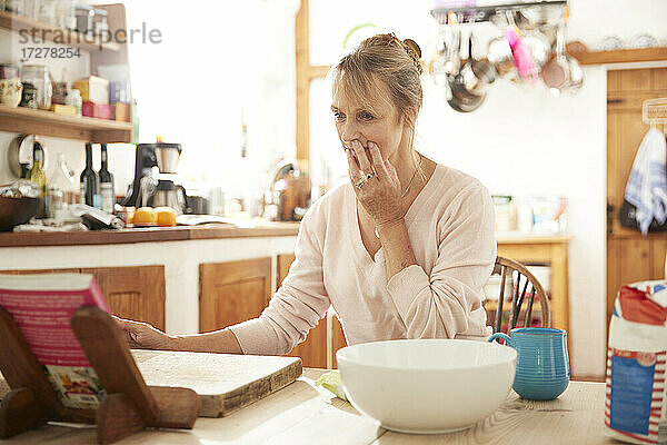 Ältere Frau  die in der Küche sitzend ein Rezeptbuch liest