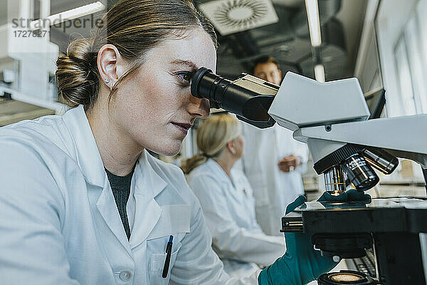 Assistentin beim Analysieren eines Objektträgers mit menschlichem Gehirn  während im Hintergrund ein Wissenschaftler im Labor sitzt