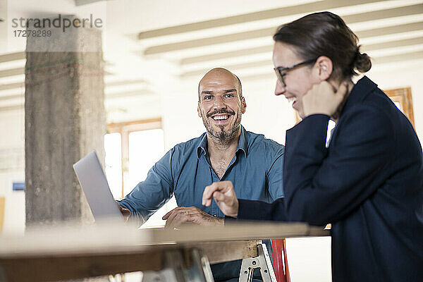 Mann lächelnd bei der Arbeit am Laptop mit Frau im Büro