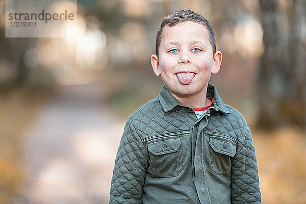 Junge streckt die Zunge heraus  während er im Herbst im Park steht