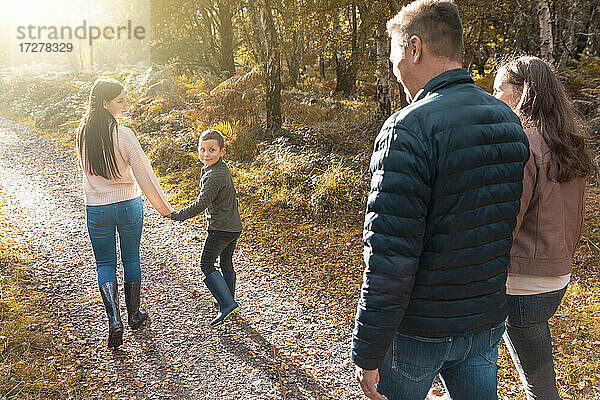 Geschwister schauen über die Schulter auf ihre Eltern  die im Herbst im Park spazieren gehen