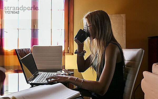 Mädchen benutzt Laptop und trinkt zu Hause Kaffee