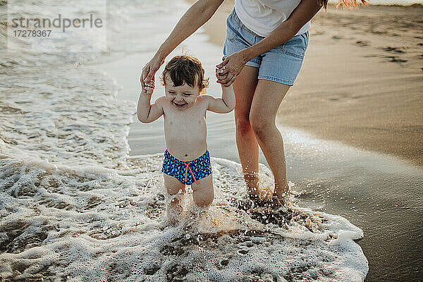 Midsection von Mutter mit Sohn genießen im Wasser am Strand an einem sonnigen Tag