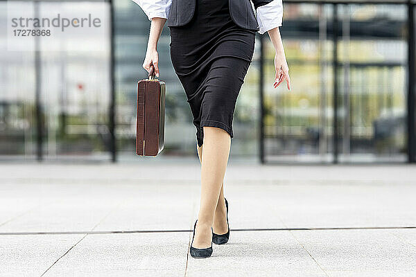Junge Geschäftsfrau mit hohen Absätzen und Aktentasche auf dem Fußweg